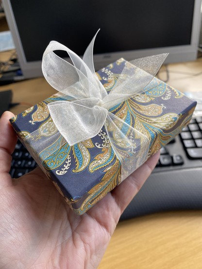 A small box in a lovely decorative leaf design, with a delicate cream ribbon tied around it.