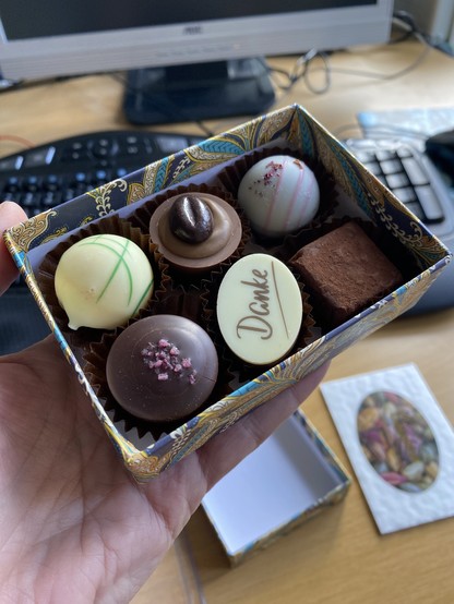 The box without its lid: inside are six individual chocolates, each one a different shape and colour. One has “Danke” written on it.