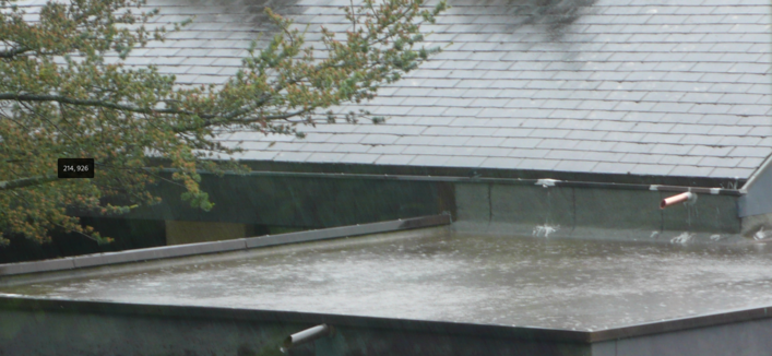 Ein Garagendach steht voll Wasser. Der Regen pladdert nur so da rein. Oben darüber ist der Ast eines Baumes zu sehen. Die Eindeckung eines Hausdachen im Hintergrund.