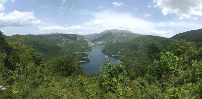 Ein zerklüfteter See umgeben von steilen Hängen, die teilweise Felsig und Bewaldet sind.