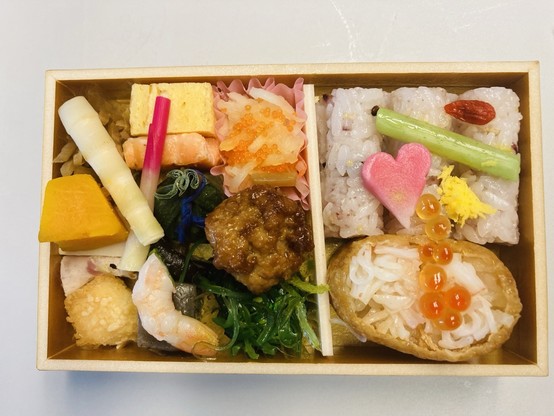 Bento Box mit vielen aus Lebensmitteln gestalten Kleinigkeiten wie Herzen und Tütchen liegt auf dem Tisch eines Shinkansen