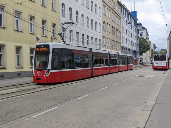 Rot-weiße Flexity-Straßenbahn der Wiener Linien vor Häuserzeile, daneben ein Bus