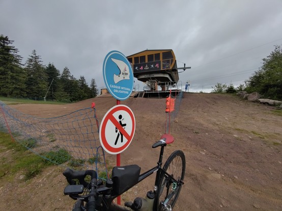 Die Bergstation von Lac Blanc. Mein Fahrrad steht neben einem Schild, was einen Integralhelm voraussetzt und ein Verbots Schild für Fußgehende.
