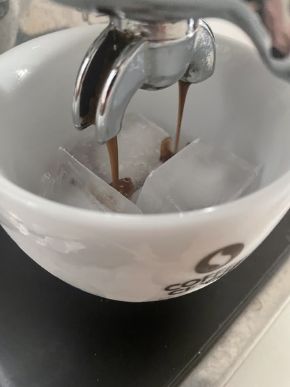 Espresso being made from a machine, directly into a cup full of ice cubes.
