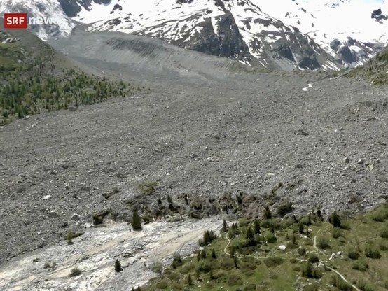Screenshot eines Videos, das bei einem Helikopterüberflug gedreht wurde: Unterhalb des Gletscherkars hat sich ein Geröllfeld ausgebreitet. Im Vordergrund sichtbar die vom Geröll nun überdeckte Landschaft des alpinen Hochtals.