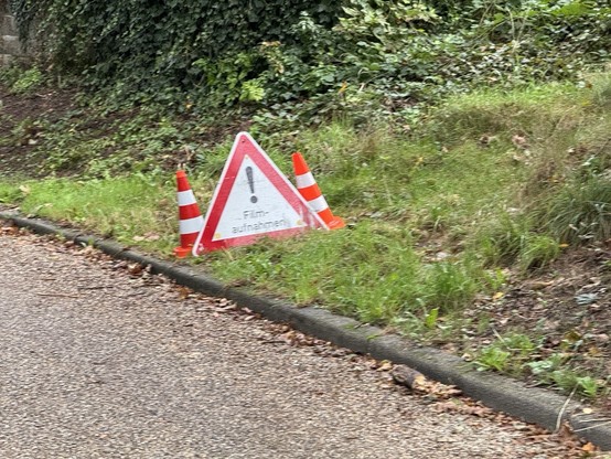 Am Straßenrand steht ein Warnschild mit der Aufschrift „! Filmaufnahmen“