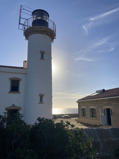 Blick auf einen Leuchtturm und ein eingeschossiges Gebäude. Dazwischen das Meer.